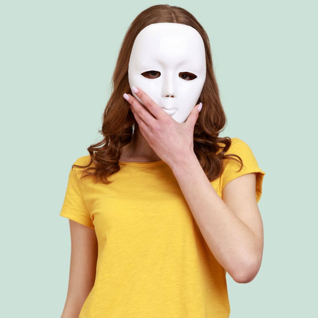 young woman in a yellow shirt hiding her face behind a white mask