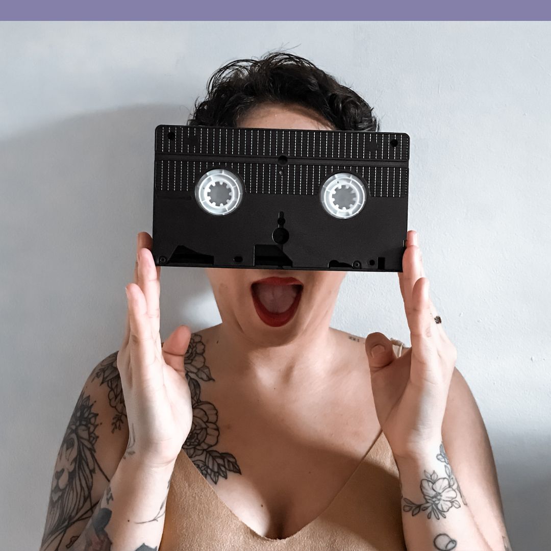 tattooed lady hiding her face behind a VHS cassette